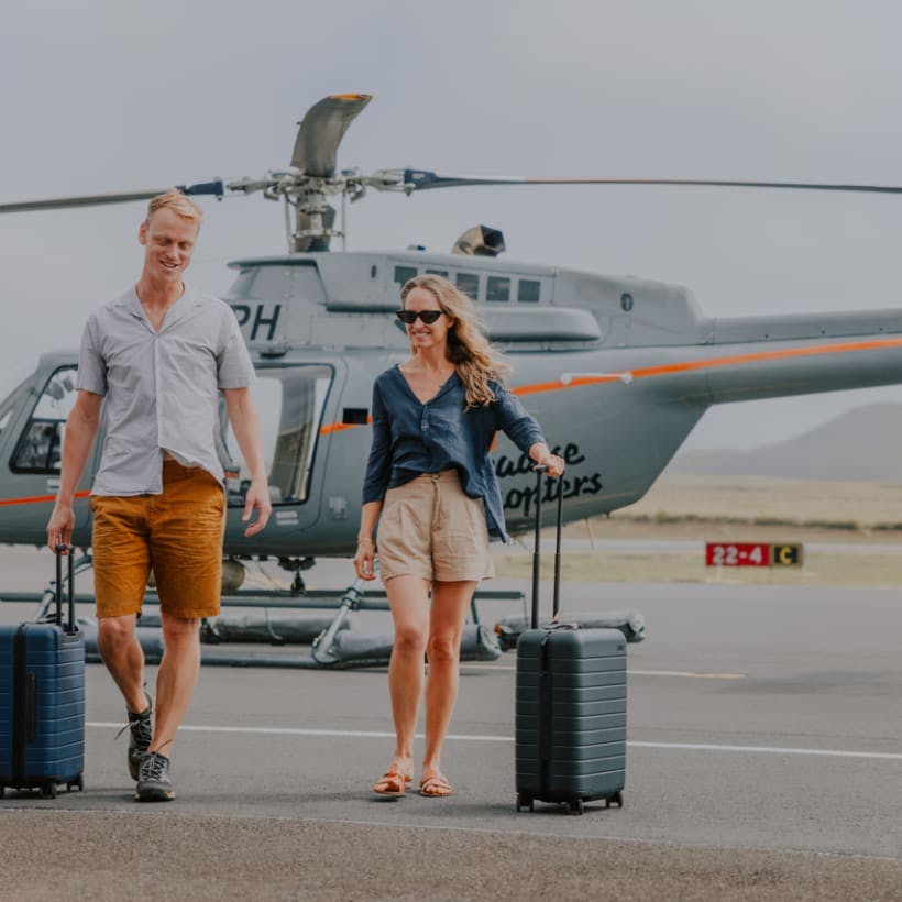 two people walking from a helicopter rolling their suitcases 