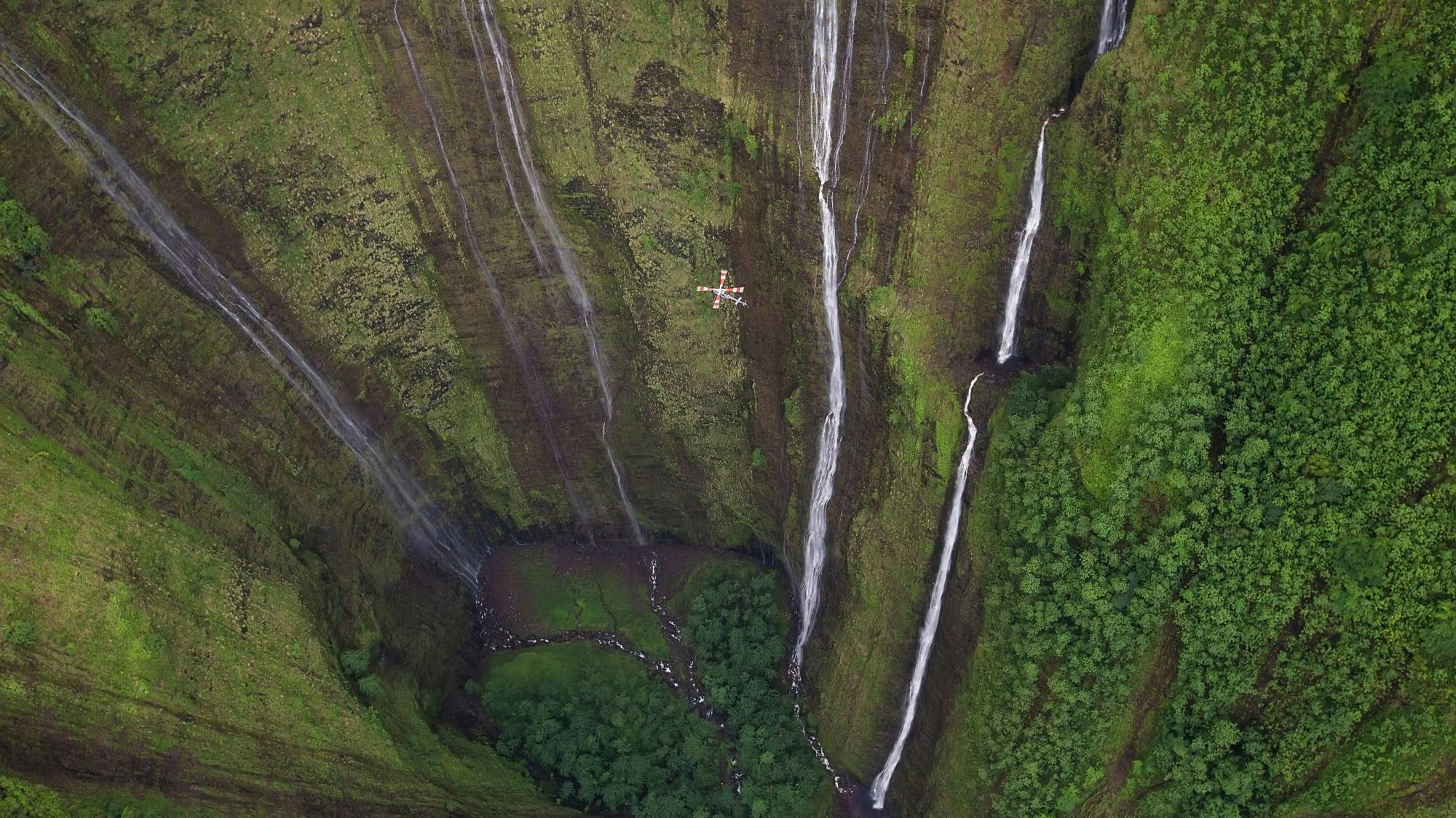 Many waterfalls with a helicopter flying adjacent to them 