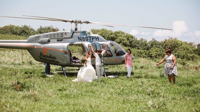 two people who are getting married holding hands, walking away from a helicopter